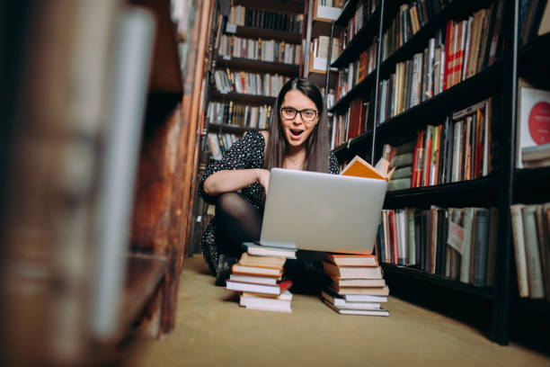 istock Sweet young student girl sitting on library floor and reading a book 1307291643