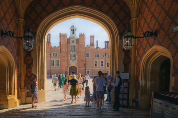 Tourists crowd the archway entrance to the historic 16th century royal residence Hampton Court Palace and courtyard on a summer day.