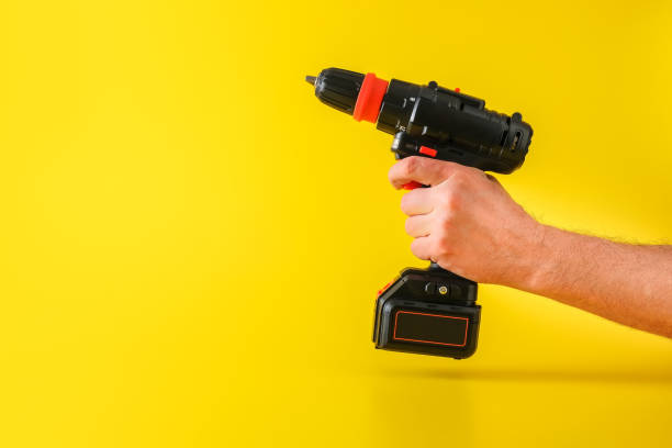 istock Cordless screwdriver on yellow background with cropped male hand 1307292736