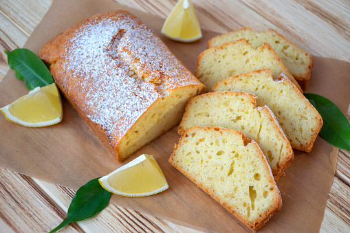 Pieces of lemon cake with full pie, lemons on rustic wooden board. Easy recipe of citrus dessert for everyday cooking.