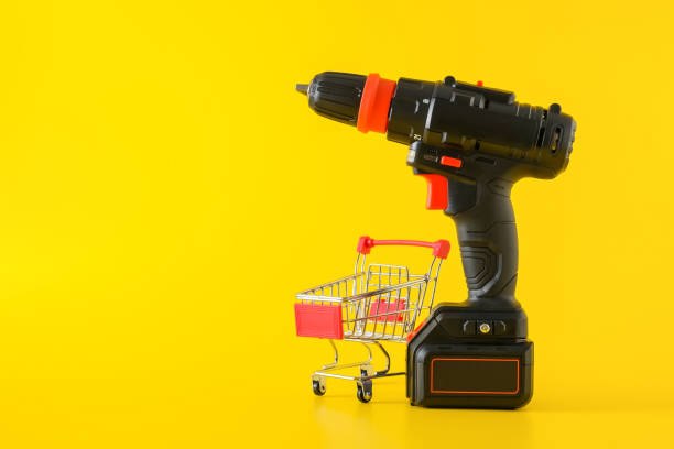 Modern black cordless screwdriver with empty shopping cart Modern black cordless screwdriver, drill with empty shopping cart on yellow background, copy space for text chuck wagon stock pictures, royalty-free photos & images