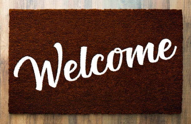 темно-коричневый приветственный коврик на фоне деревянного пола. - welcome sign doormat greeting floor mat стоковые фото и изображения