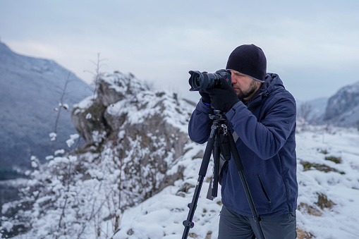 Male photographer capturing a beautiful winter view on mountain with camera and tripod