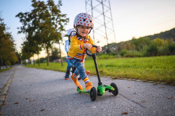 irmãos caucasianos dirigindo bicicleta balance e empurrar scooter ao ar livre - 5553 - fotografias e filmes do acervo