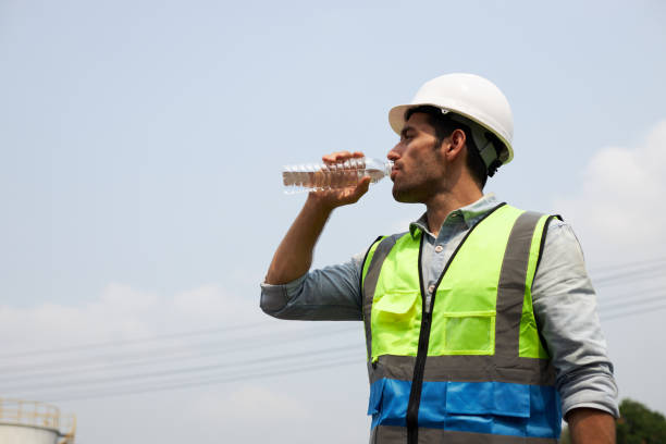 The young engineer drinks water to quench his thirst. A handsome engineer or male construction worker in protective clothing and a helmet, is drinking water to quench his thirst in the harsh sunlight. quench your thirst pictures stock pictures, royalty-free photos & images