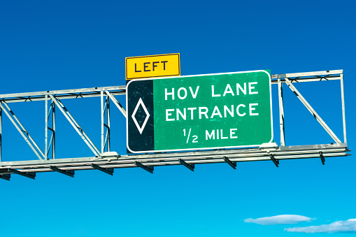 High occupancy vehicle lane entrance overhead road sign. Blue sky.