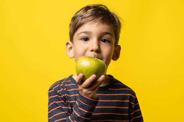 녹색 사과를 들고 노란색 현대 배경 앞에 서 작은 백인 소년 어린 아이 - child eating apple fruit 뉴스 사진 이미지