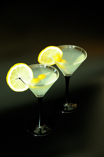 Two glasses of white vermouth with olives and lemon slices on a black background. Close-up.