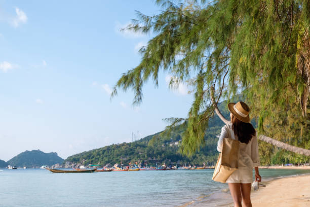 istock a woman with hat and bag strolling on the beach with blue sky background 1307321727