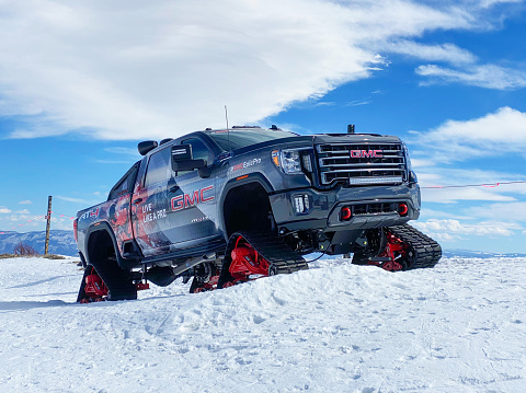 Utah, USA - March 8th, 2021: Custom built GMC Pick up Sierra HD AT4 All Mountain with snow tracks instead of wheels, parked on top of a hill in Park City ski resort.