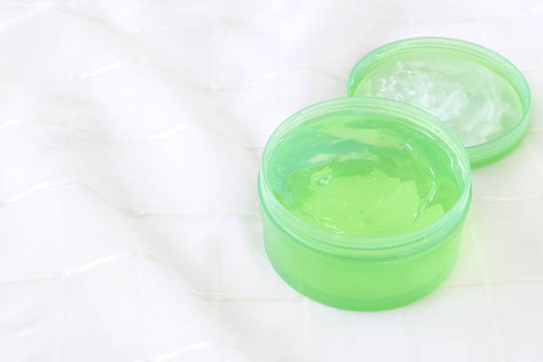 da vicino crema gel verde (gel di aloe vera) in contenitore di plastica su sfondo tessuto bianco, vista laterale, aspetto morbido, avere spazio di copia. - merchandise spa treatment botanical spa treatment exfoliation foto e immagini stock