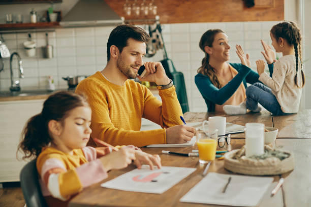 istock Smiling working father taking notes during phone call while being with his family at home. 1307328083
