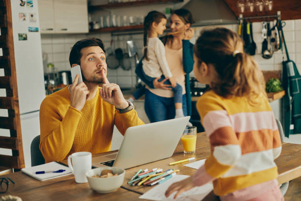 Please be quiet, I have an important business call! Mid adult father silencing his daughter while talking on mobile phone and working at home. working at home with children stock pictures, royalty-free photos & images