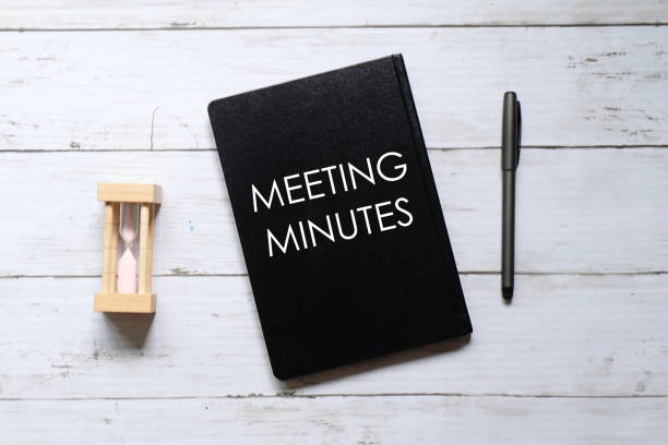 Top view of hour glass,pen and notebook written with 'MEETING MINUTES' on white wooden background. stock photo