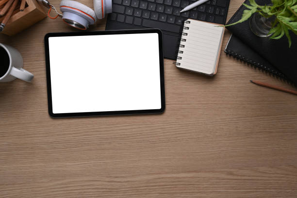 istock Top view of mock up digital tablet with whit screen, notebook, keyboard, headphone and copy space on wooden table. 1307338308