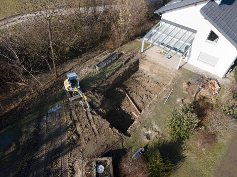 Drones aerial view of a construction site of a pool, small yellow excavator digs hole for pool and is almost finished in a nice garden in austria