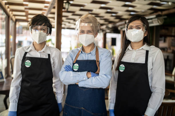 istock Restaurant owner and waitresses working at a restaurant, wearing a double protective face masks and a badge showing that they are vaccinated against COVID-19. 1307341352