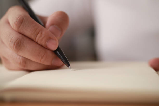 istock Close up of hand holding pen and writing on empty book paper, selective focus 1307341421