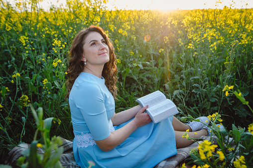 Christian girl holds bible in her hands. Reading the Holy Bible in a field during beautiful sunset. Concept for faith, spirituality and religion. Peace, hope