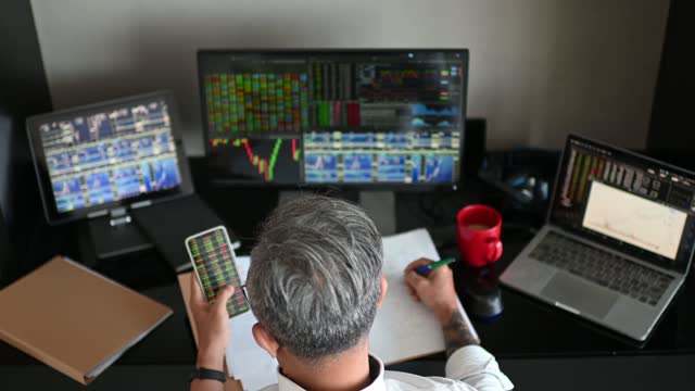 high angle rear view asian chinese working senior working from home multiple computer monitor screen with stock exchange data