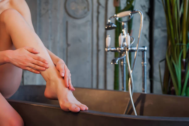 le mani delle donne fanno il massaggio ai piedi con olio cosmetico per applicare gocce sulla pelle nella vasca da bagno - self massage foto e immagini stock