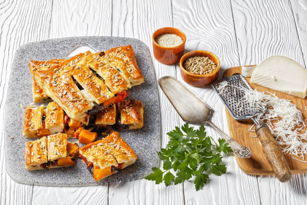 tarte américaine de pâte feuilletée de légumes avec le fromage de chèvre garni de graines de tournesol et de sésame remplies de légumes rôtis servis sur un fond en bois blanc, vue supérieure, plan rapproché - puff pastry pumpkin garlic cheese photos et images de collection