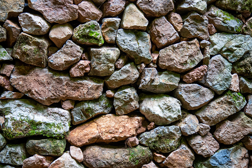 Old wall built by stacking unevenly sized rocks covered with moss, background pattern