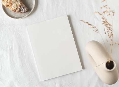 Empty blank white magazine cover mock up, ceramic vase with dried grass and croissant on plate. Flat lay. Top view. Copy space