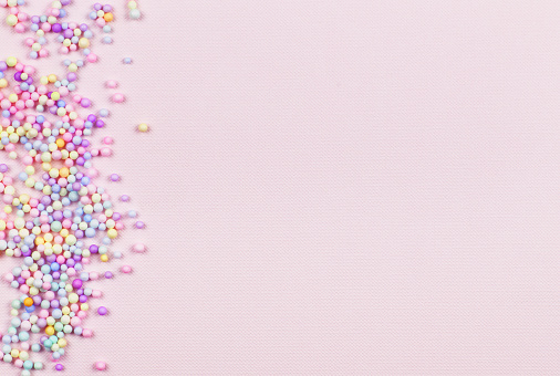 Small colorful pastel balls in a border on pink paper background