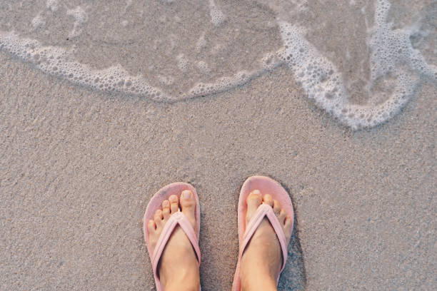 ноги женщины носить тапочки стоять на песке тропический пляж с морской водой всплеск фона. - flip flop human foot sand women стоковые фото и изображения