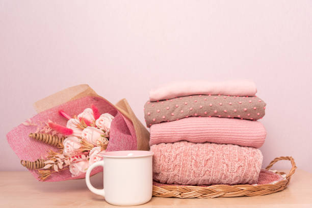 istock Stack of folded wool knitted sweaters or pullovers in pink pastel colors and mag on table with flowers bouquet 1307355043