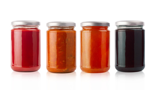 front view of set of small jam and vegetable jars in different colors without labels and shiny metallic lid covers isolated on white background