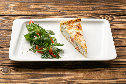 Quiche with tomatoes and arugula on a white ceramic plate