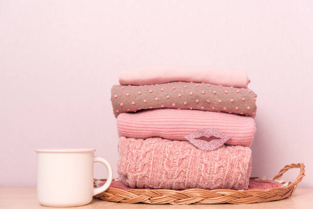 istock Stack of folded wool knitted sweaters or pullovers in pink pastel colors on table with cup of tea. 1307361538