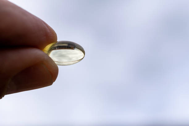 ビタミンd、指は、青い空の背景とカプセルを保持 - fish oil healthy eating capsule isolated ストックフォトと画像