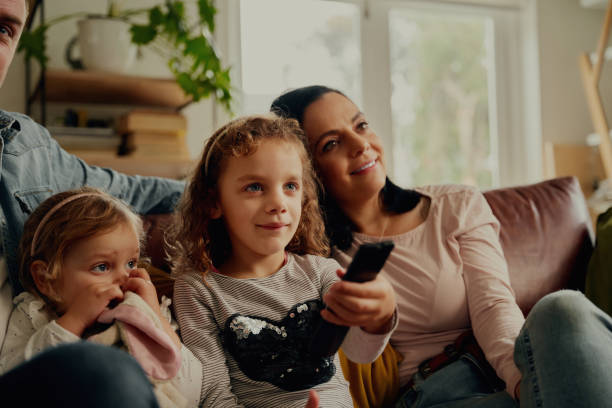 istock Happy girl watching television controlling while controlling remote and sitting with family on couch 1307362811