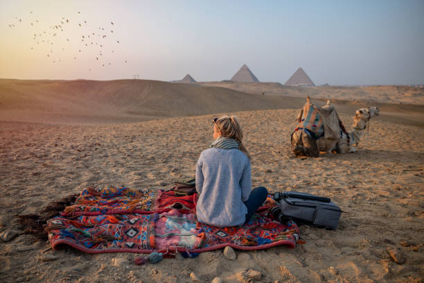 Woman watches sunset at the Giza Pyramids, she looks across the Sahara desert Rear view of a female tourist enjoying a tour to the Pyramids of Giza in Egypt. dromedary camel photos stock pictures, royalty-free photos & images