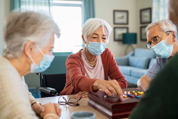 Senior people playing chinese checkers during covid19 lockdown Senior woman wearing face mask and playing chinese checkers at home during covid-19 pandemic. Old woman with surgical face mask for safety against covid19 playing with friends at nursing home. Elderly people enjoy a board game at care facility centre. chinese checkers stock pictures, royalty-free photos & images