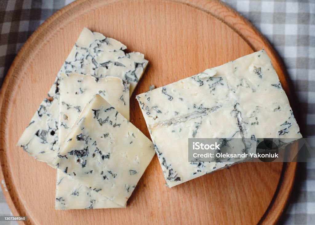Sliced cheese with blue mold on a wooden cutting board. Cheese composition. Top view. Cheese texture with mold. Stilton Cheese Stock Photo