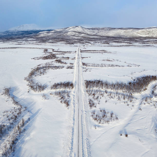A long straight road leading through a snowy landscape in the mountaineous area near the Kebnekaise massif in the Scandinavian Mountains.