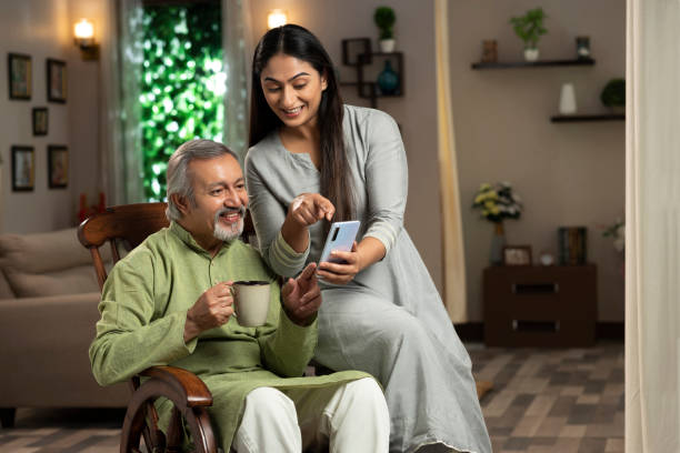 自宅でロッキングチェアに座っている若い女性と彼女の成熟した父親の肖像画。彼女は携帯電話で何かを示している:- ストック写真 - father indian ethnicity india love ストックフォトと画像
