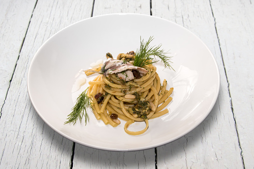 spaghetti bucatini with sardines - Sicilian recipe with raisins, pine nuts and fennel,in white dish on  white colored wooden boards