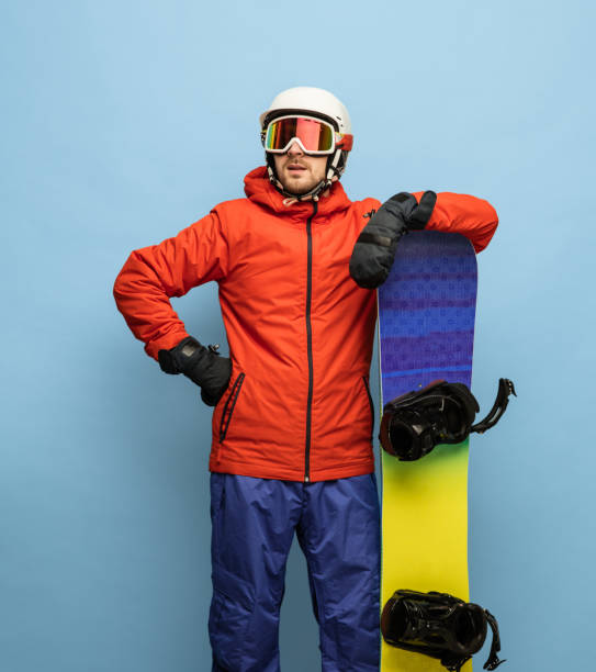 istock Young man in bright ski suit and snowboard isolated on blue background. 1307378556