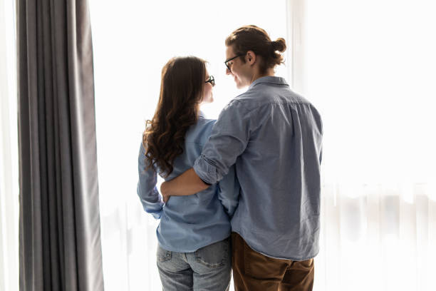 istock Back view of young couple looking out the window and hugging while having a breakfast at home 1307378585