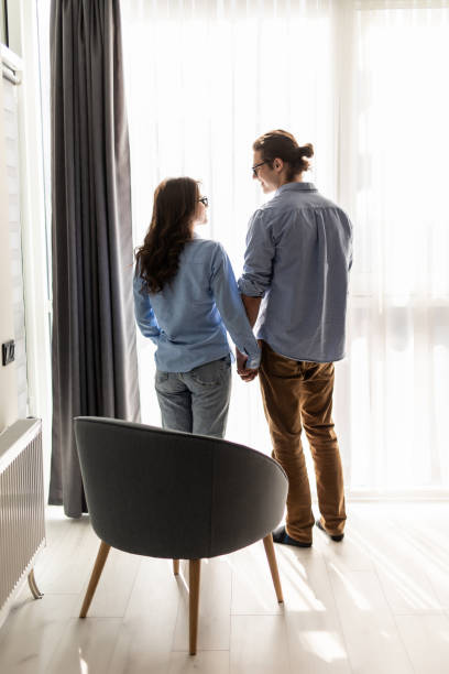 istock Back view of young couple looking out the window and hugging while having a breakfast at home 1307379650