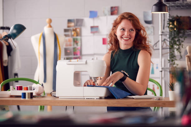 istock Smiling Female Student Or Business Owner Working In Fashion Using Sewing Machine In Studio 1307384945