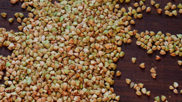 trigo-sarraceno verde não penteado é derramado em uma mesa de madeira marrom em uma pequena pilha - buckwheat groats - fotografias e filmes do acervo