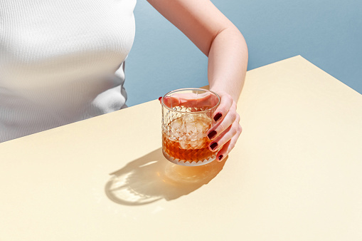 Glass with Whiskey and Ice Cube in Woman Hand on Table on Blue Background. Modern Isometric Style. Creative Concept.
