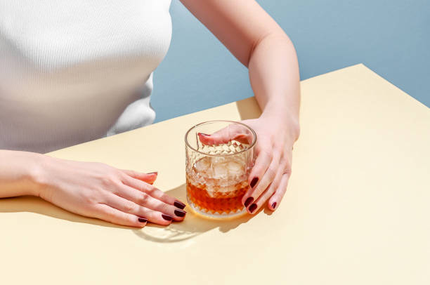 istock Glass with Whiskey and Ice Cube in Woman Hands on Table on Blue Background. Modern Isometric Style. Creative Concept 1307386516