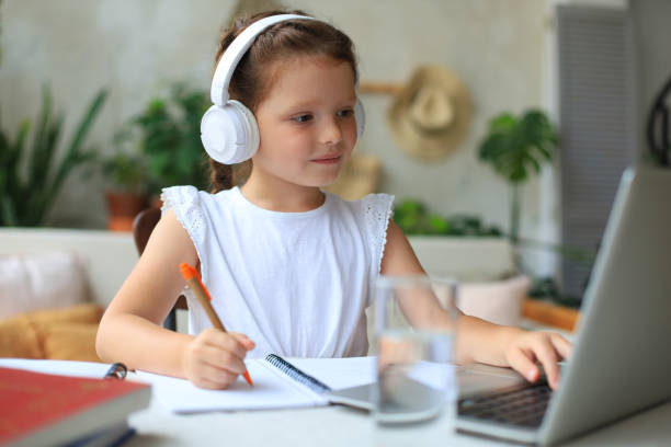 smiling little girl in headphones handwrite study online using laptop at home, cute happy small child in earphones take internet web lesson or class on pc. - 24120 imagens e fotografias de stock